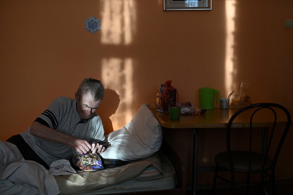 Житель дома престарелых открывает пакет со сладостями.