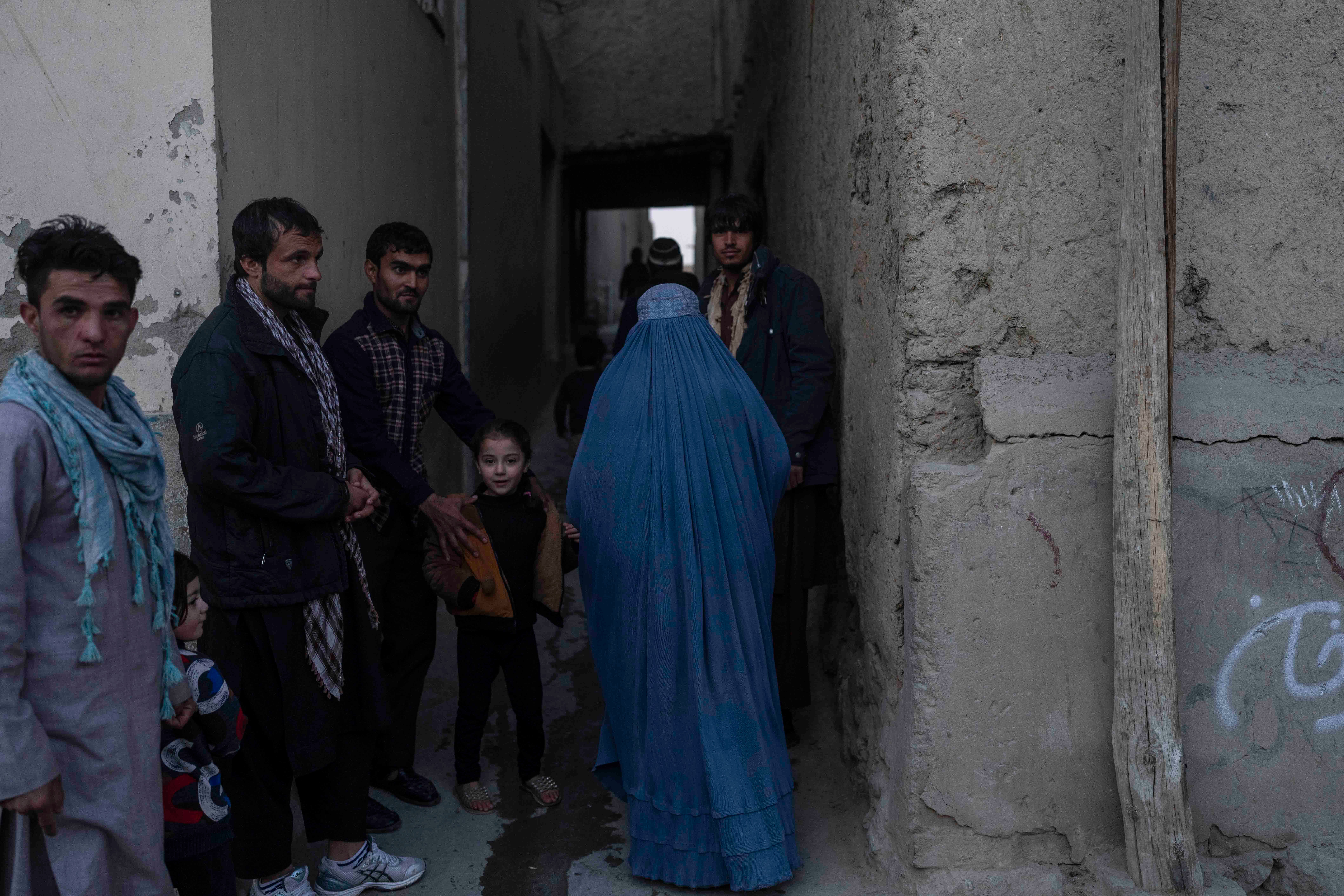 A woman wearing a burqa walks by a group of men 