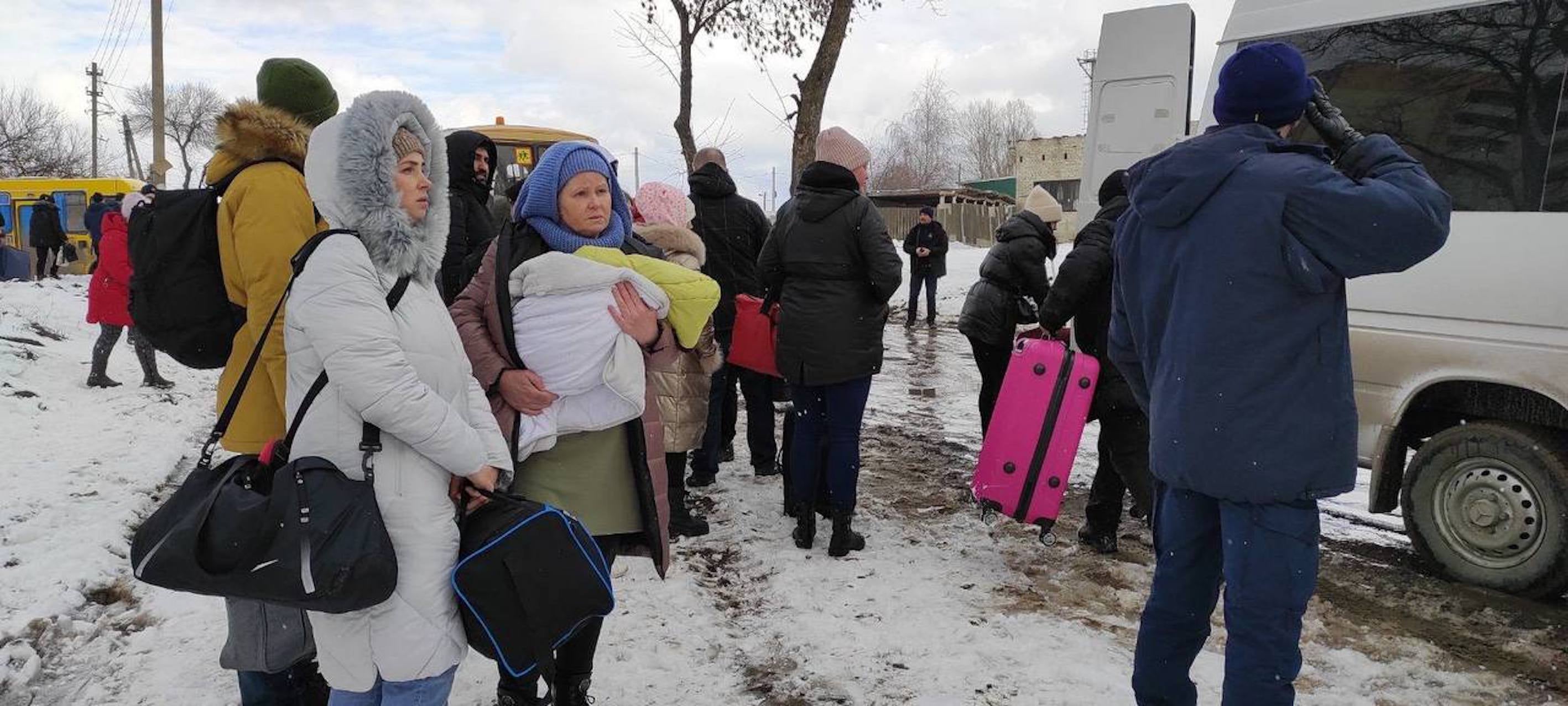 People hold their belongings as they wait to get into a van