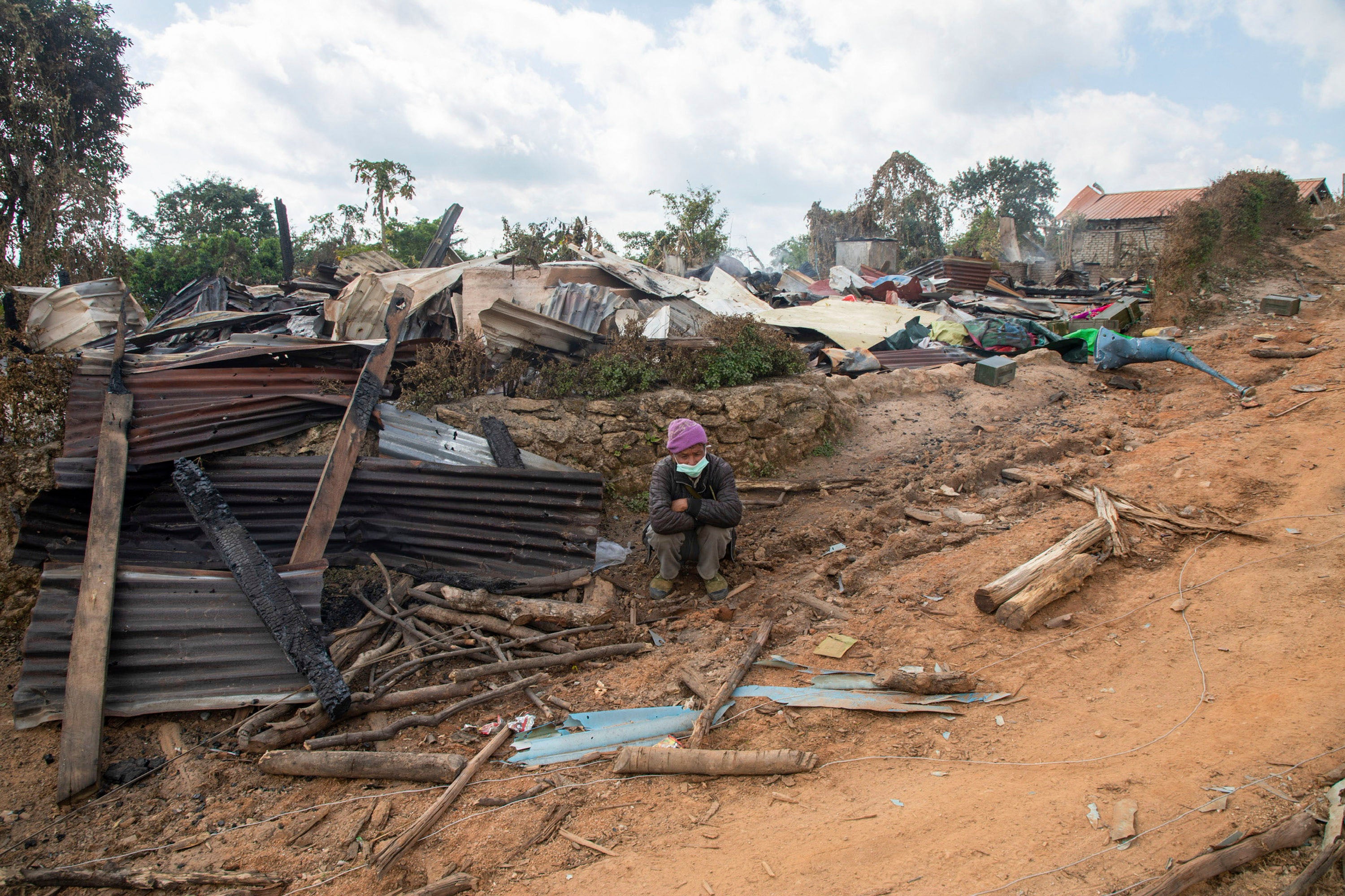 Seorang pria duduk di depan sebuah rumah di negara bagian Shan yang rusak akibat pertempuran antara pasukan keamanan Myanmar dan Tentara Pembebasan Nasional Ta'ang, 10 Januari 2023.