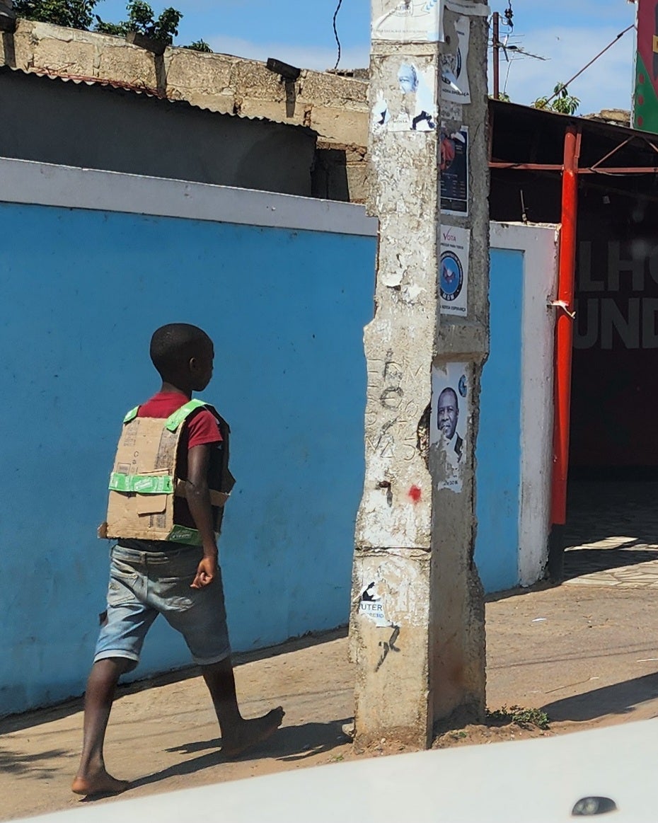 Ein Junge trägt eine „kugelsichere Weste“ aus Pappkarton, während er am 5. November 2024 durch die Straßen von Maputo, Mosambik, läuft.