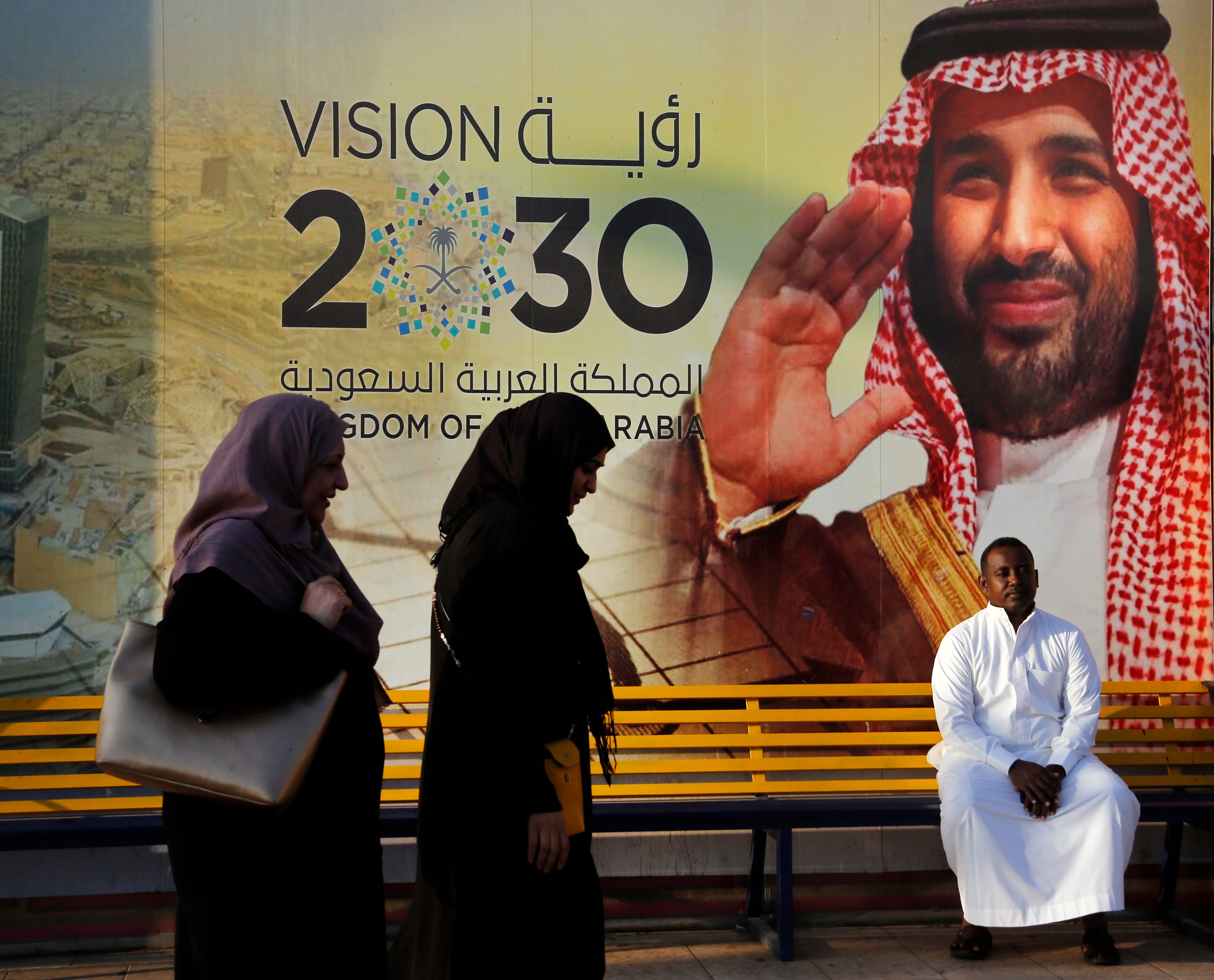 People walk past a banner showing Saudi Crown Prince Mohammed bin Salman that reads "Vision 2030"