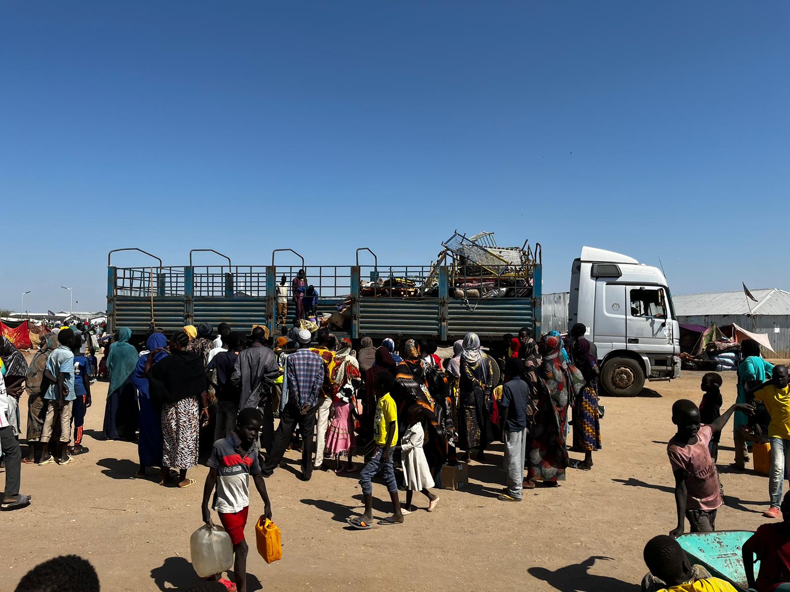Menschen steigen aus einem Laster, der sie von der Grenze zum Sudan zum Transitlager in Renk im Südsudan gebracht hat. Man sieht nur ein paar Koffer und Bettgitter.