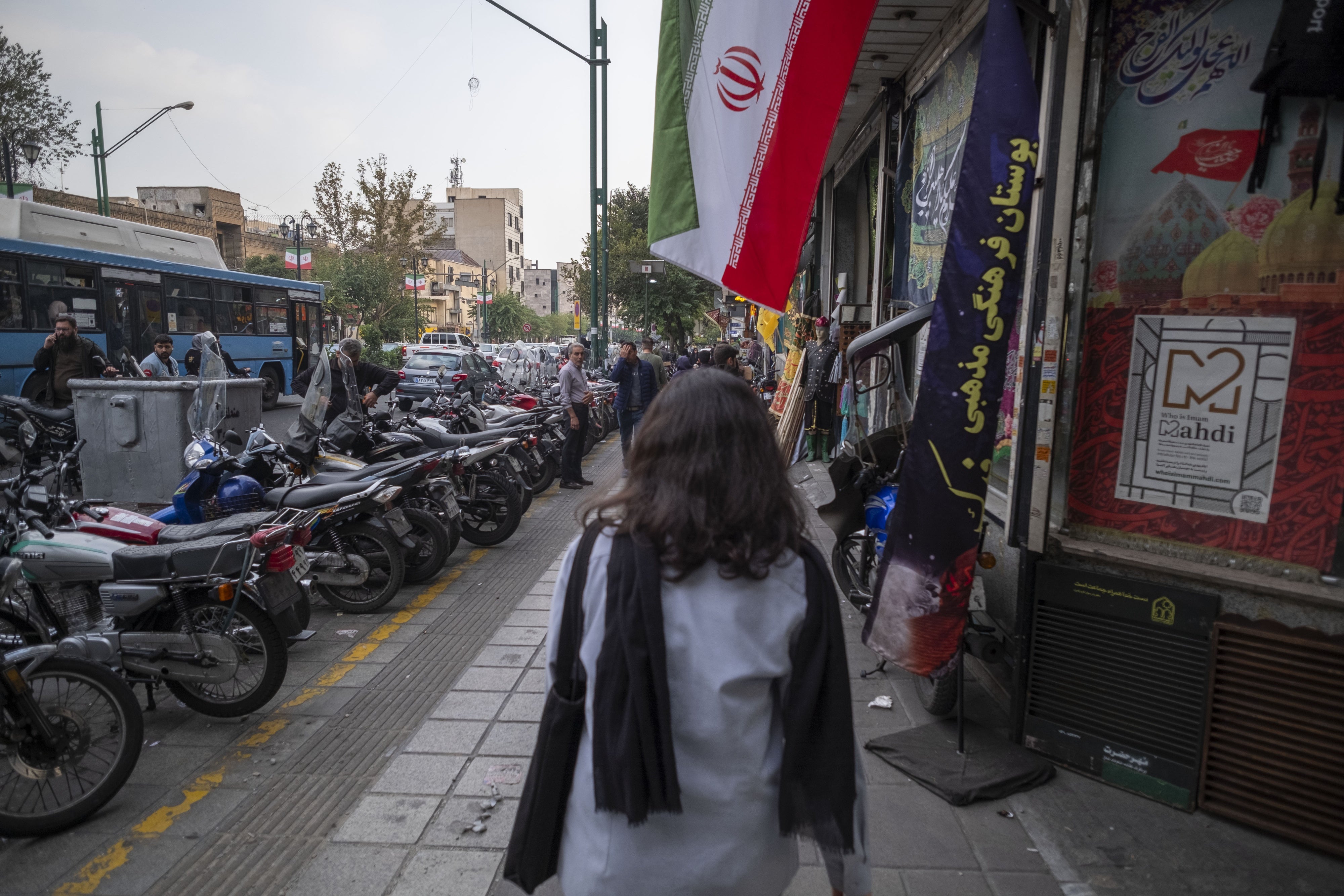شابة إيرانية لا ترتدي الحجاب الإلزامي تسير تحت علم إيراني في وسط طهران، إيران، في 29 سبتمبر/أيلول 2024.