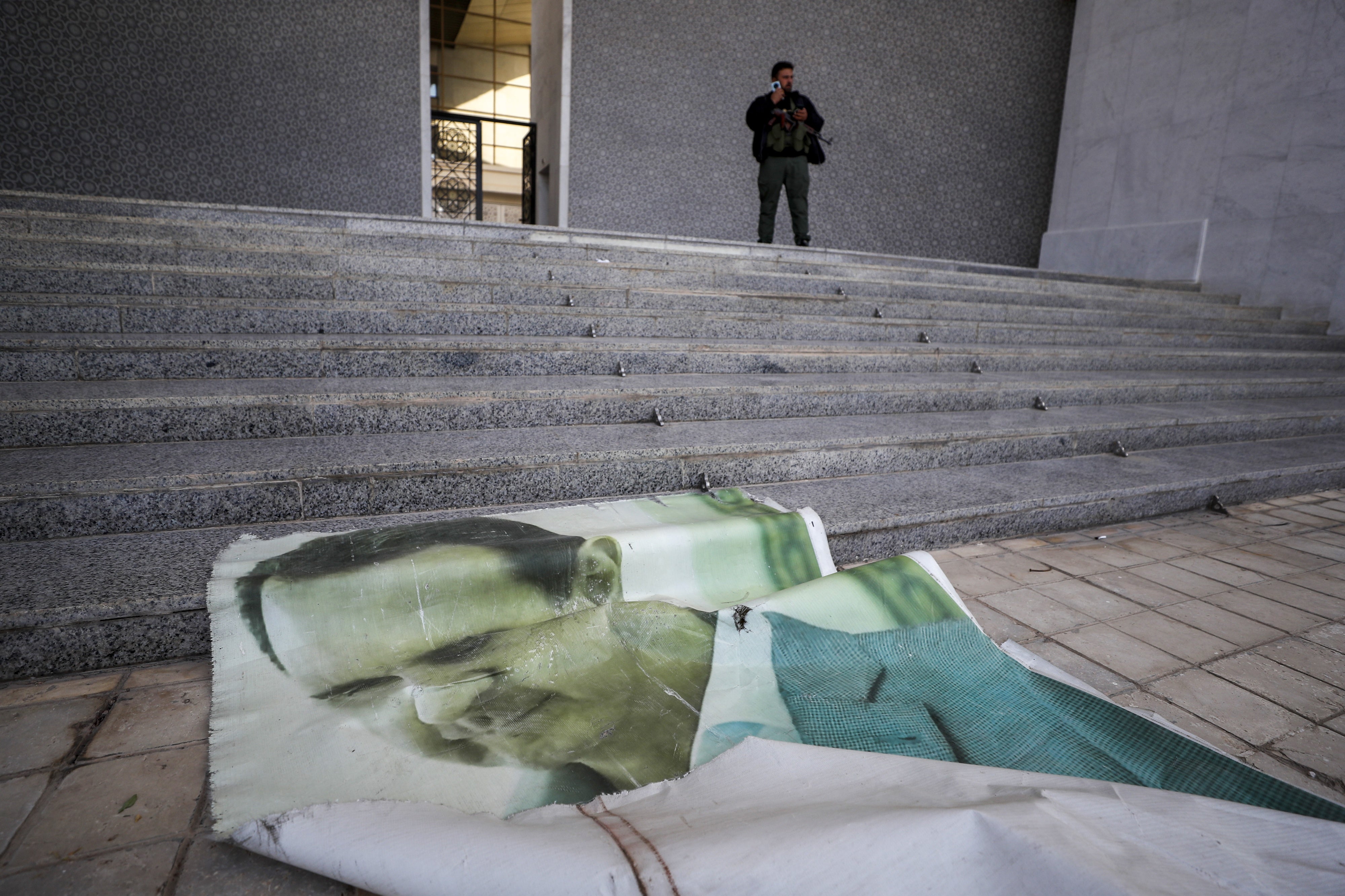 Une photo géante du président syrien déchu, Bashar al-Assad, était déroulée sur le sol du palais présidentiel à Damas, le 8 décembre 2024 ; en haut des marches, un combattant d’un groupe armé d’opposition surveillait les lieux.
