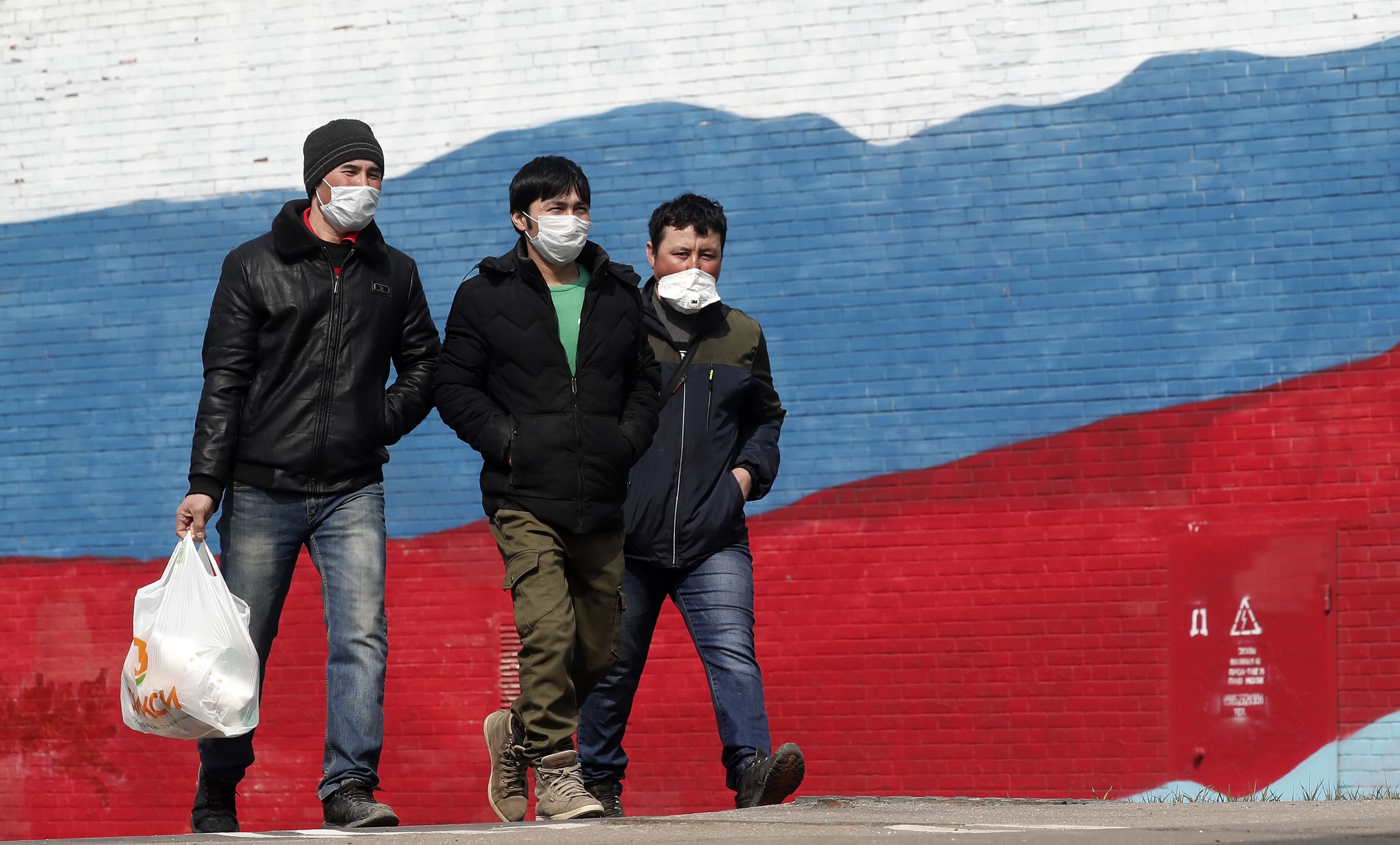 Trois hommes portant des masques de protection marchent devant une fresque représentant le drapeau russe