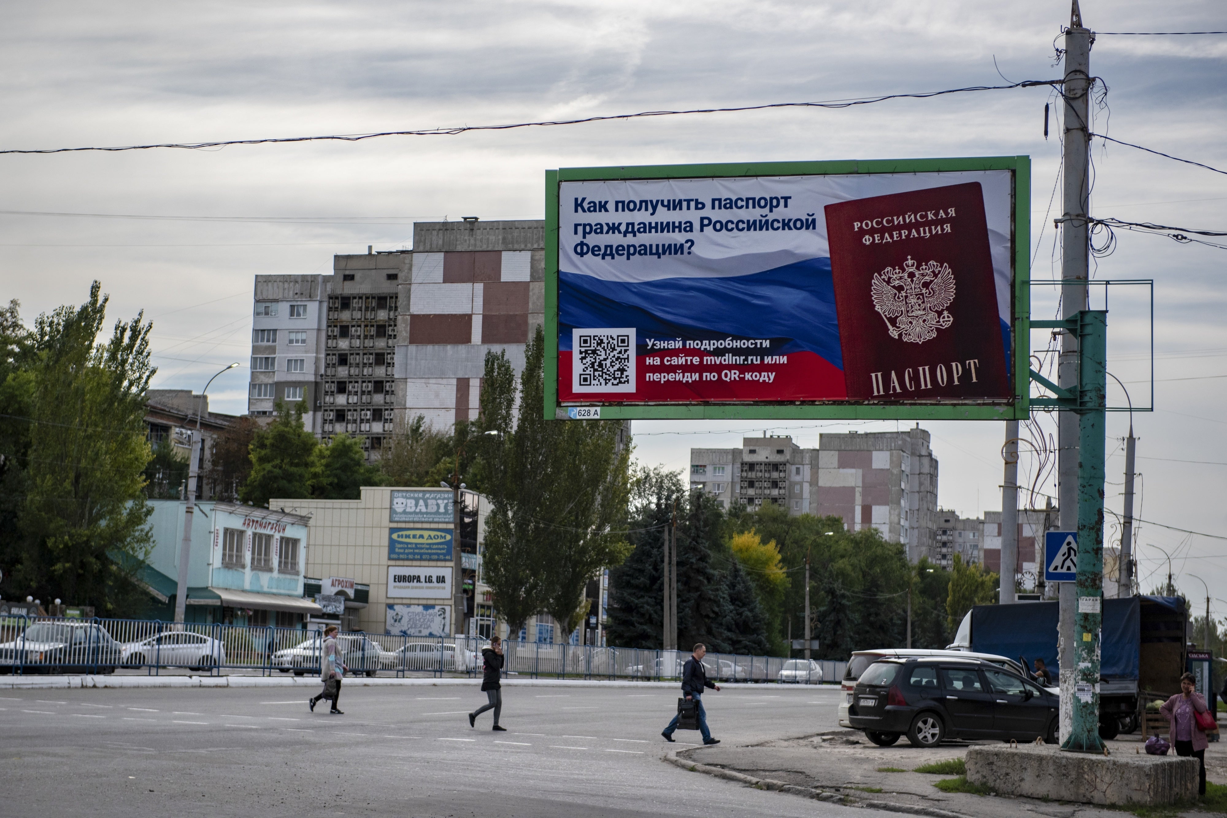 Des personnes traversent une rue avec un panneau indiquant « Comment obtenir un passeport de citoyen russe » dans le territoire occupé de Louhansk, le 22 septembre 2022.