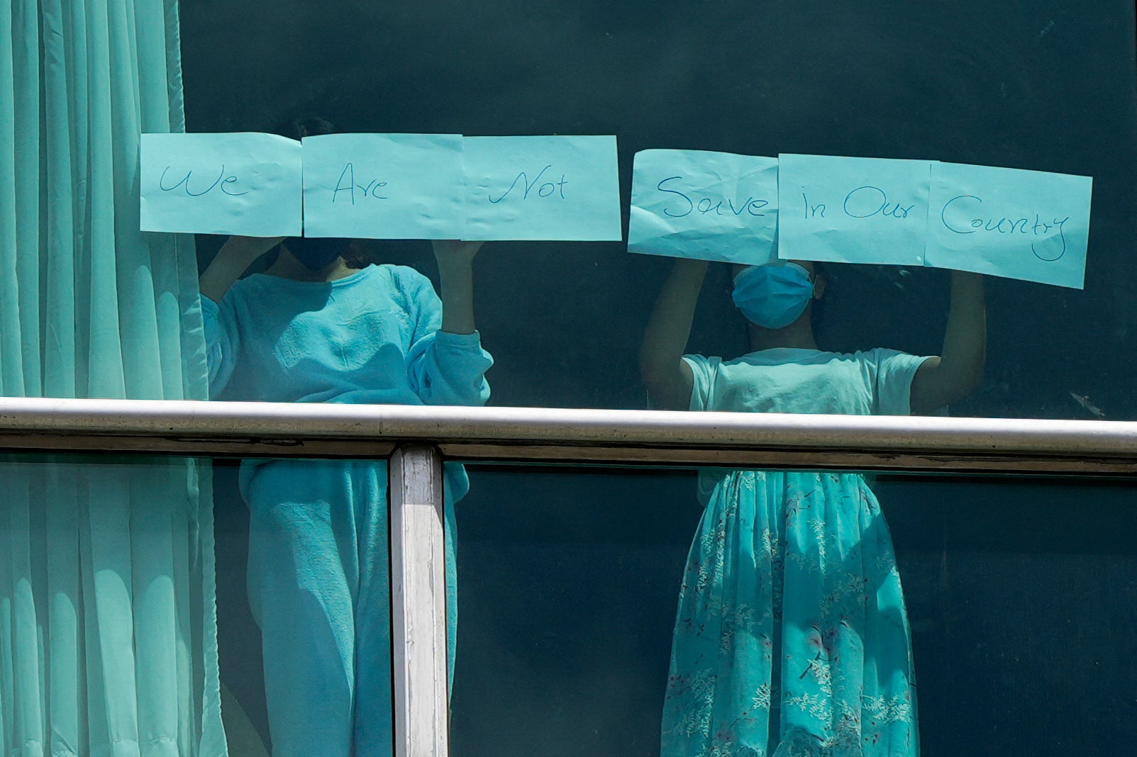 Migrants expelled from the US hold up papers that read “We are not safe in our country” in the window of a hotel