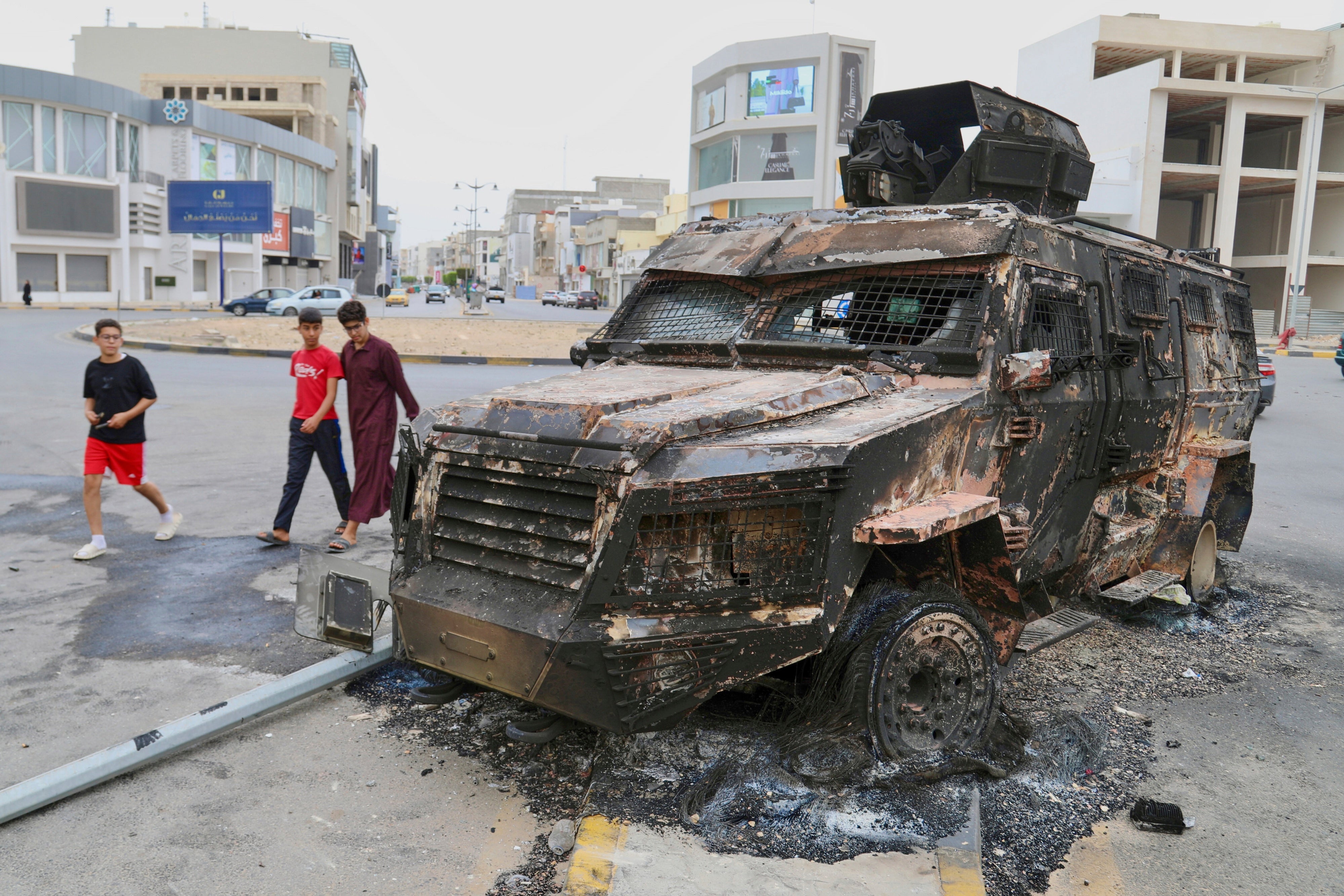 ثلاثة صِبية يسيرون بجانب مدرعة محترقة.