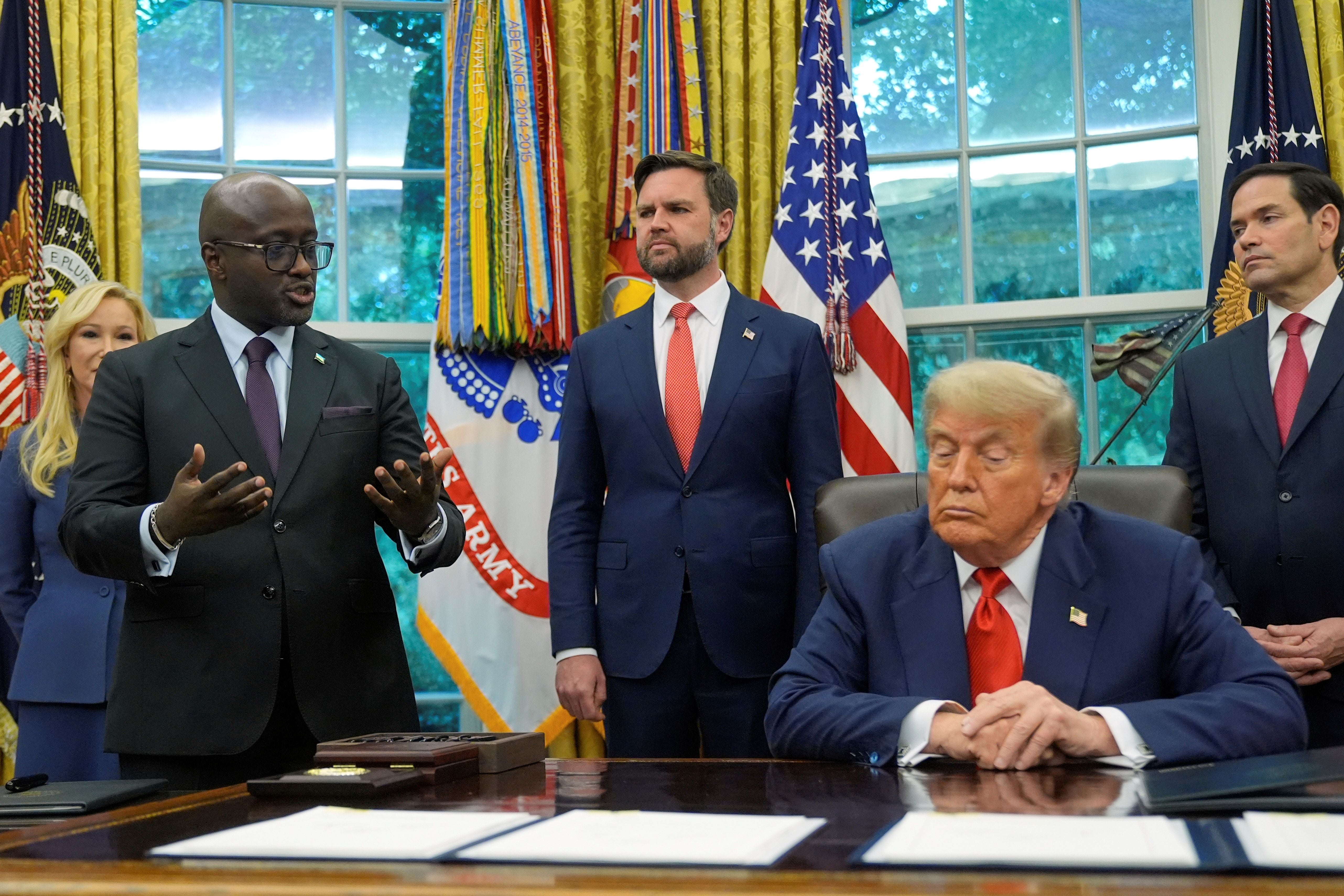 President Trump sitting in the Oval Office surrounded by aides 