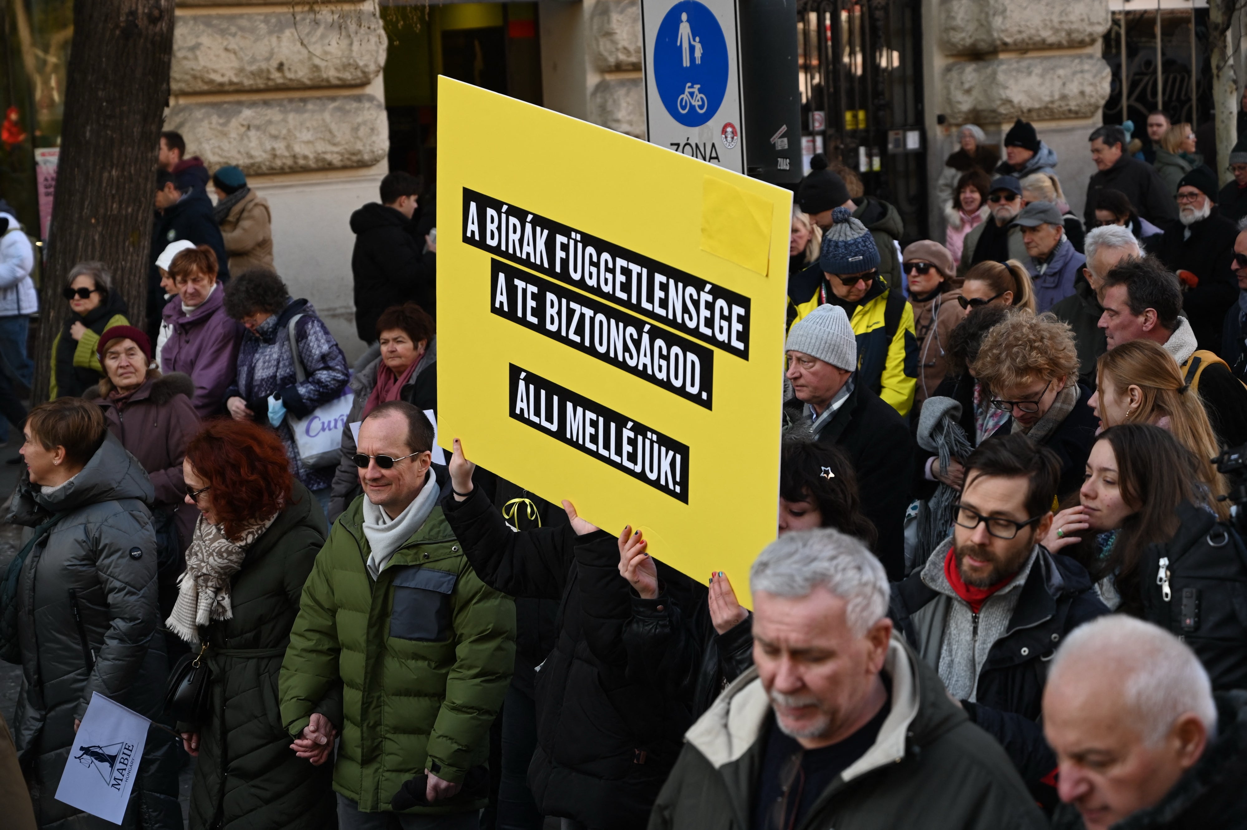 Résztvevők egy „A bírák függetlensége a te biztonságod – Állj melléjük!” feliratú táblát tartanak, miközben magyar bírák és bírósági alkalmazottak demonstrálnak Budapesten 2025. február 22-én az igazságszolgáltatás függetlenségéért, a jogállamiságért és a bírák véleménynyilvánítási szabadságáért.