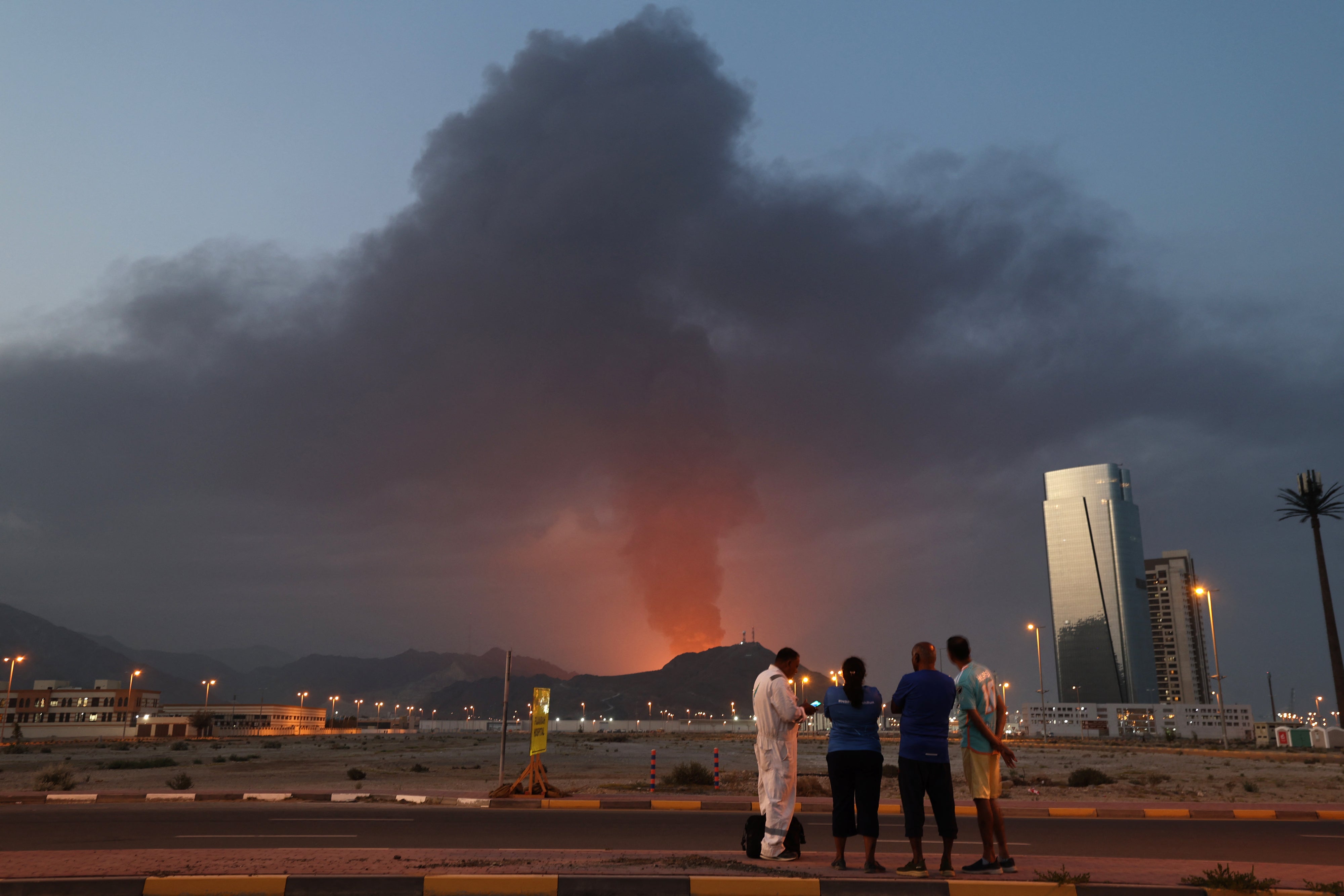 Des travailleurs étrangers regardaient un énorme panache de fumée noire visible dans le ciel à la suite d’une explosion, suspectée d’être causée par un drone iranien, dans la zone industrielle de Fujairah aux Émirats arabes unis, le 3 mars 2026. 