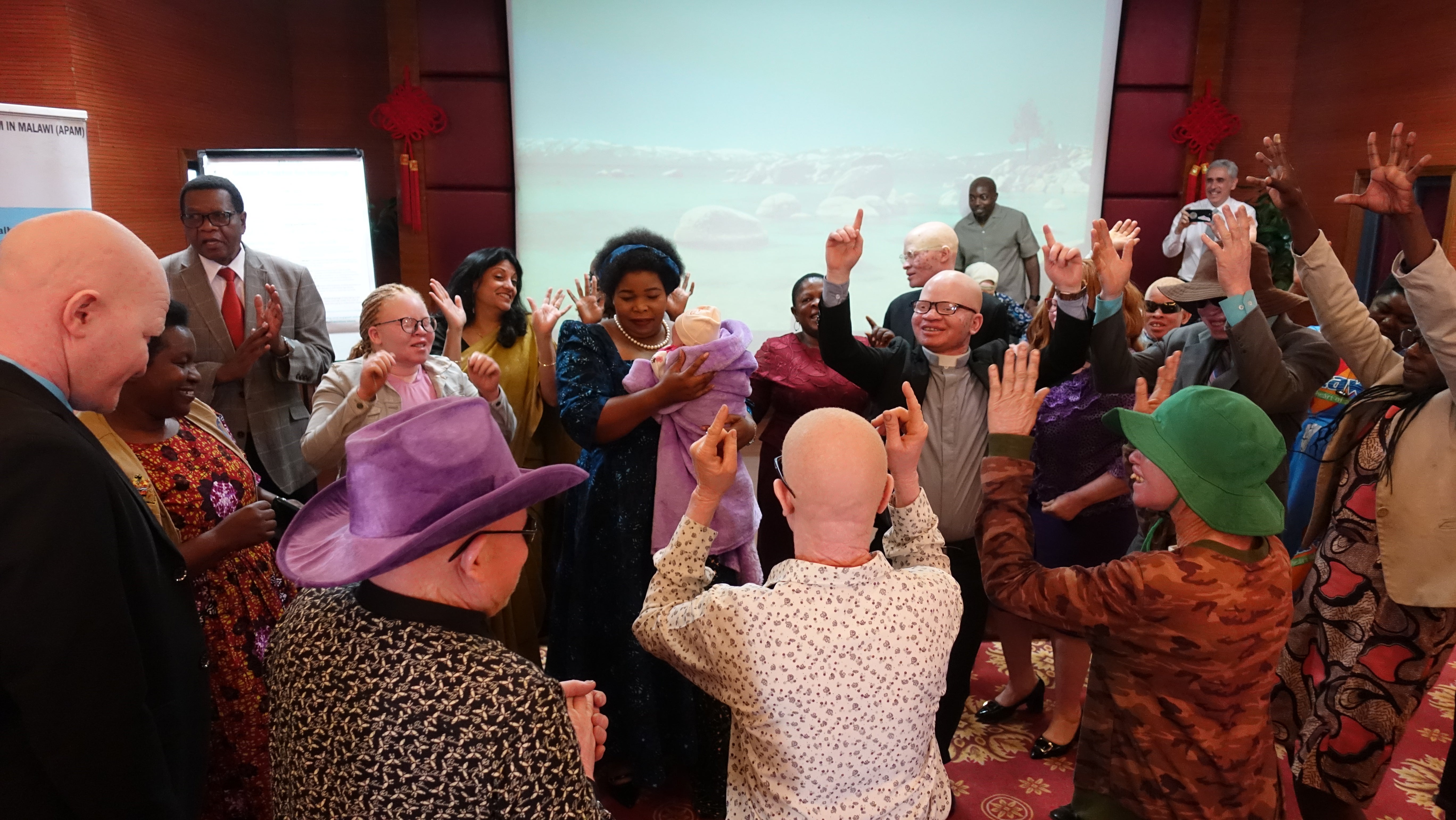 During the June 12 launch of the joint report by Human Rights Watch and African Albinism Network on discrimination against people with albinism in employment, Malawi’s Minister of Gender, Children, Disability and Social Welfare dances with a young child with albinism as community members gather around them on the eve of International Albinism Awareness Day in Lilongwe. 