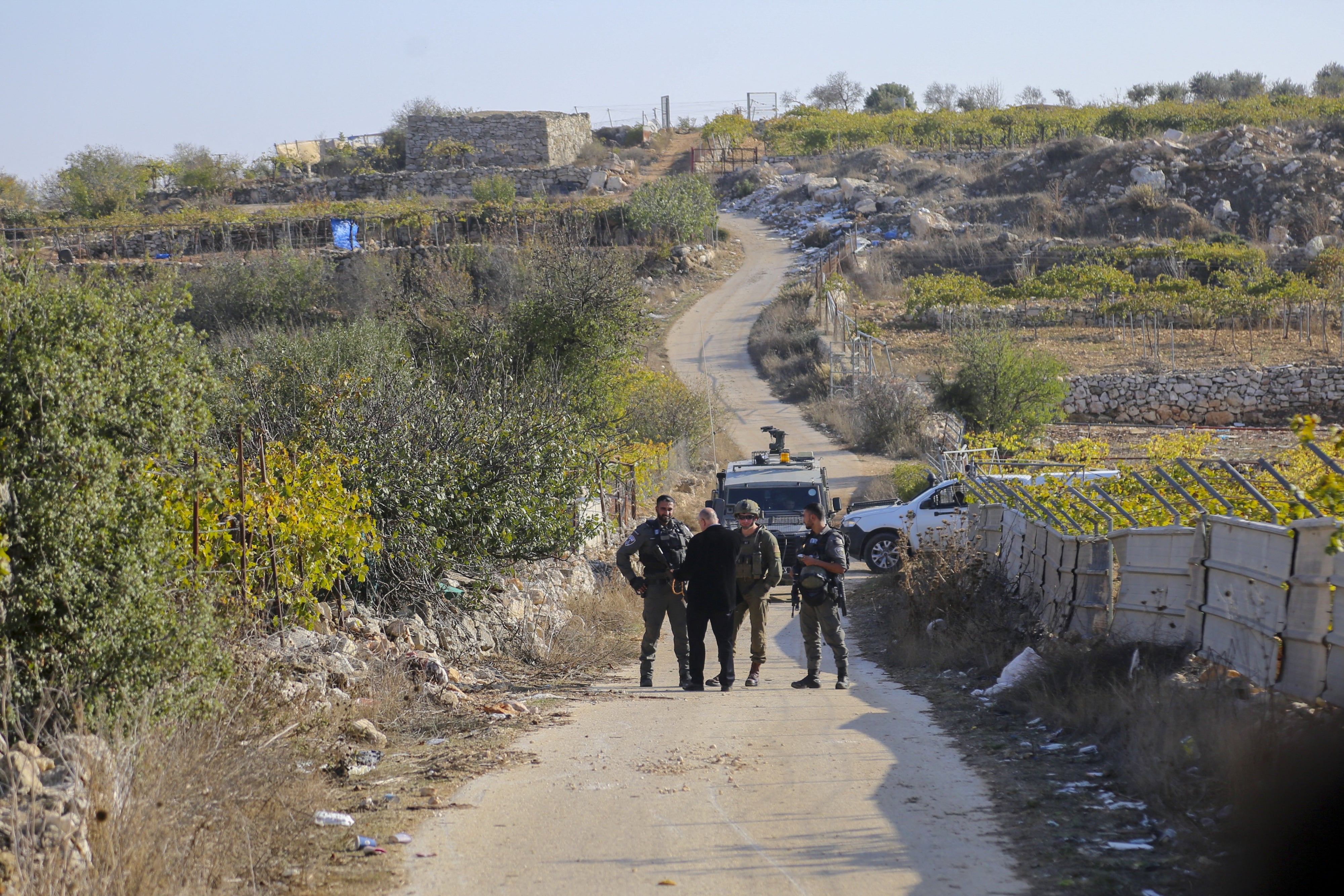 Palestinians stand behind a barrier as Israeli forces block farmers from accessing their lands in Halhul town near Hebron, in the occupied West Bank, on November 20, 2025.