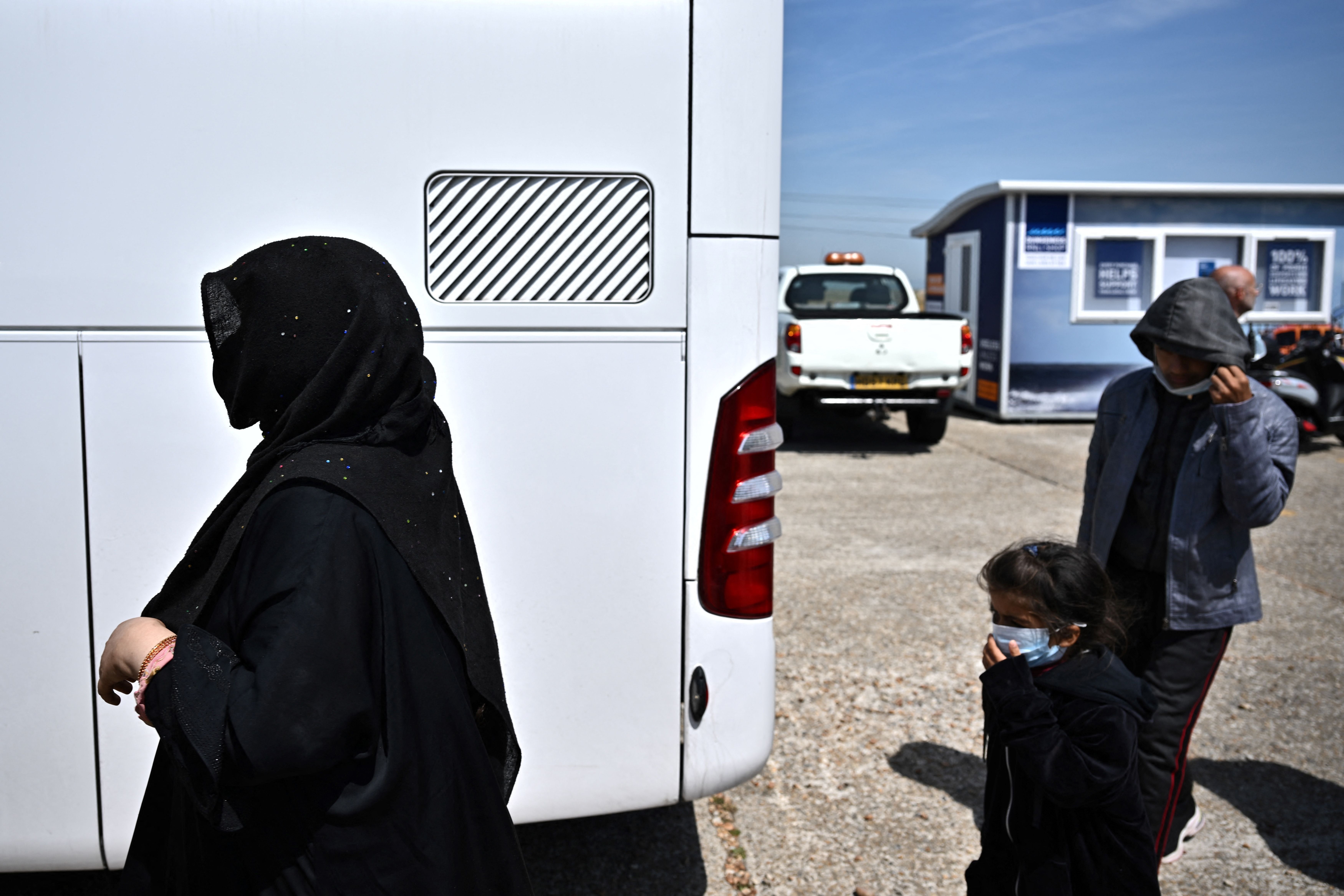 Migrants walk towards a bus to be taken for processing after disembarking from a Royal National Lifeboat Institution (RNLI) lifeboat on a beach after crossing the English Channel, in Dungeness, England, on June 15, 2022.