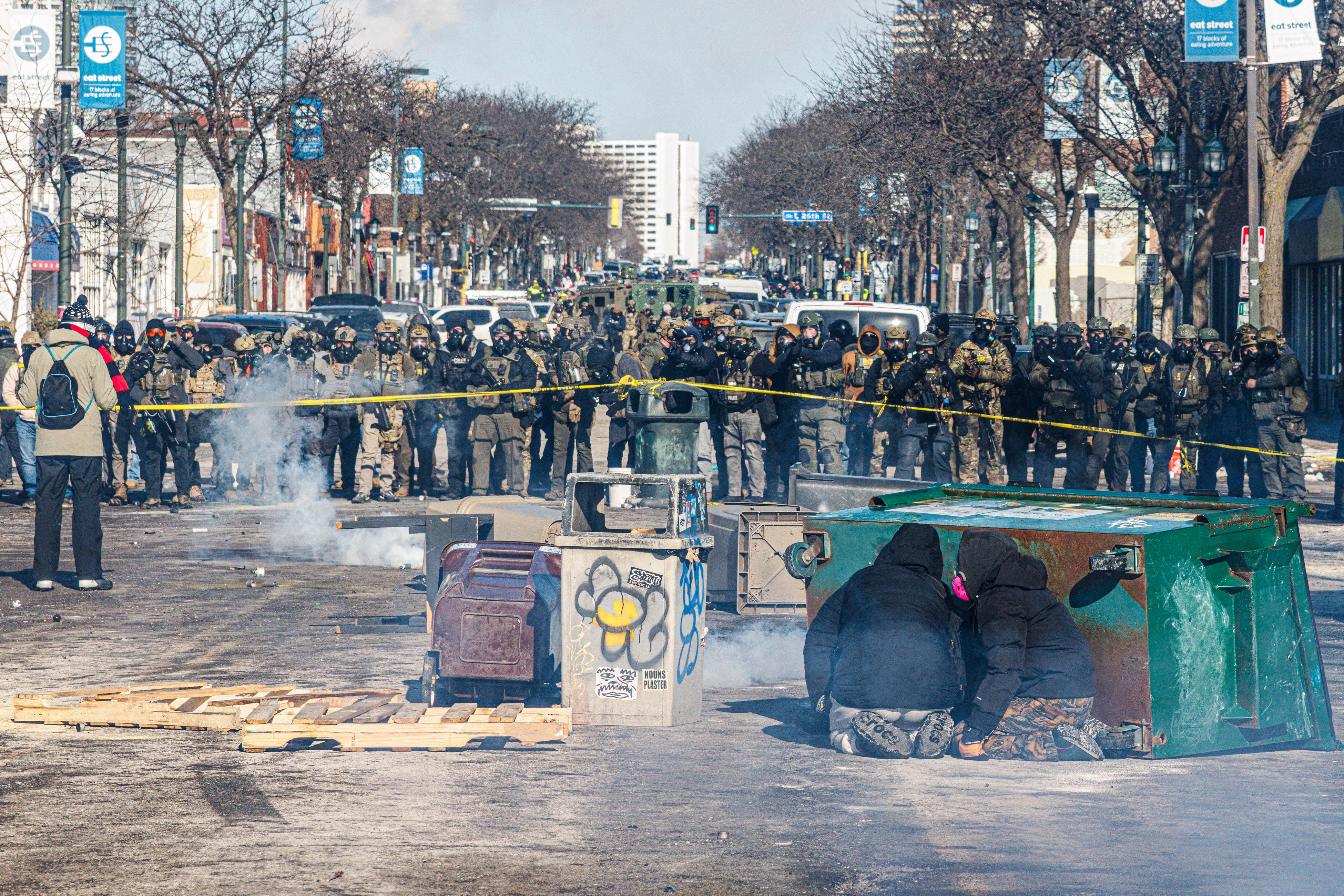 Protesters take cover behind overturned trash containers as a line of federal agents forms a barricade