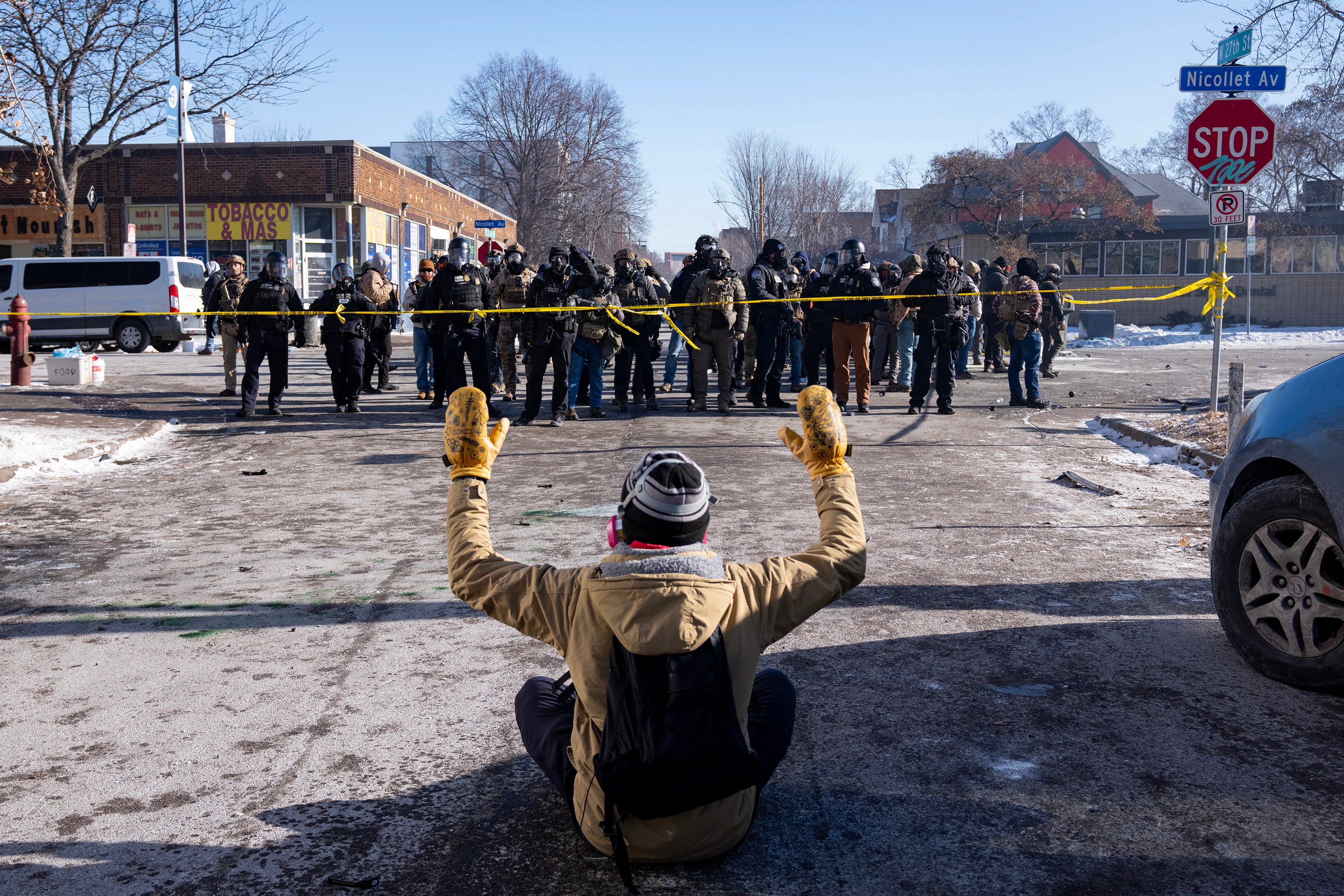 A protester sits on the street with his arms up in front of federal agents and Minneapolis Police