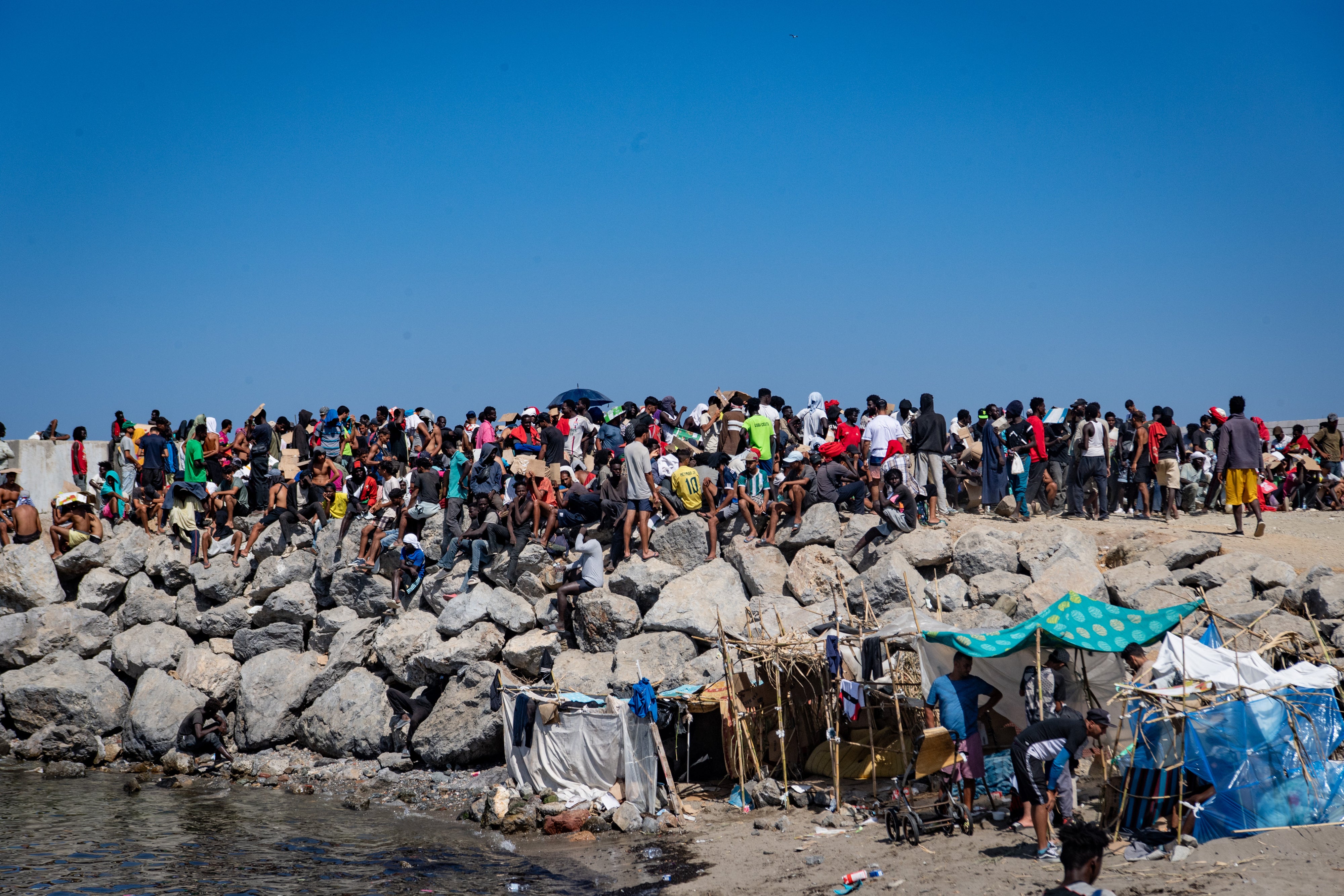 Migrants and asylum seekers gather for the once-daily food distribution at Trampolín beach