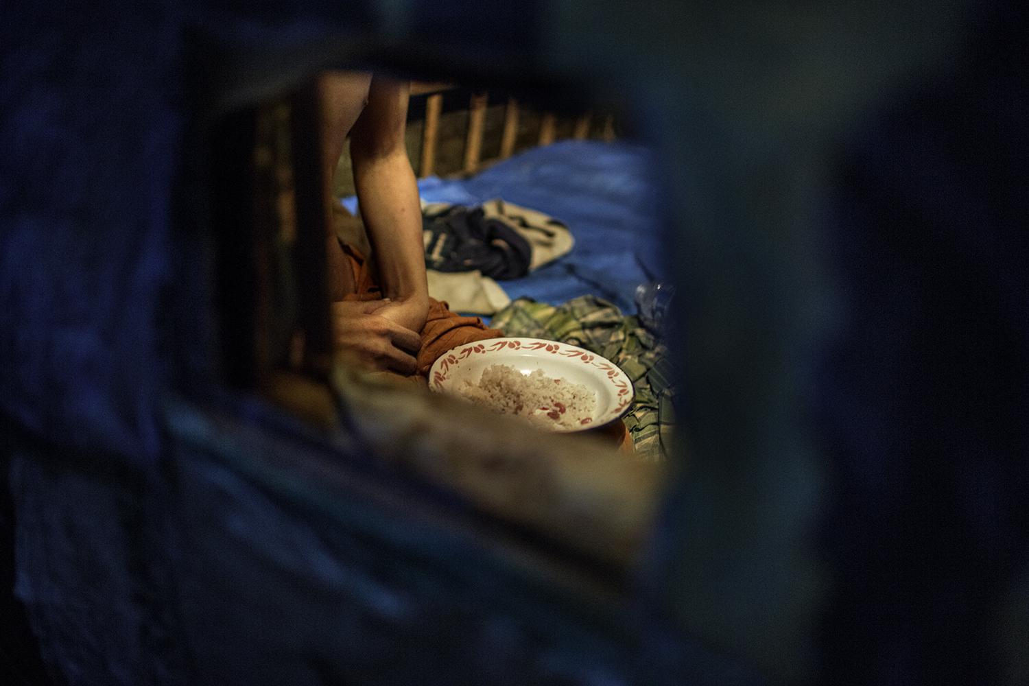 Ekram, a man with a psychosocial disability, eats his dinner in a shed outside the family home where he has been locked up. His family gives him food and water through a small hole in the shed.