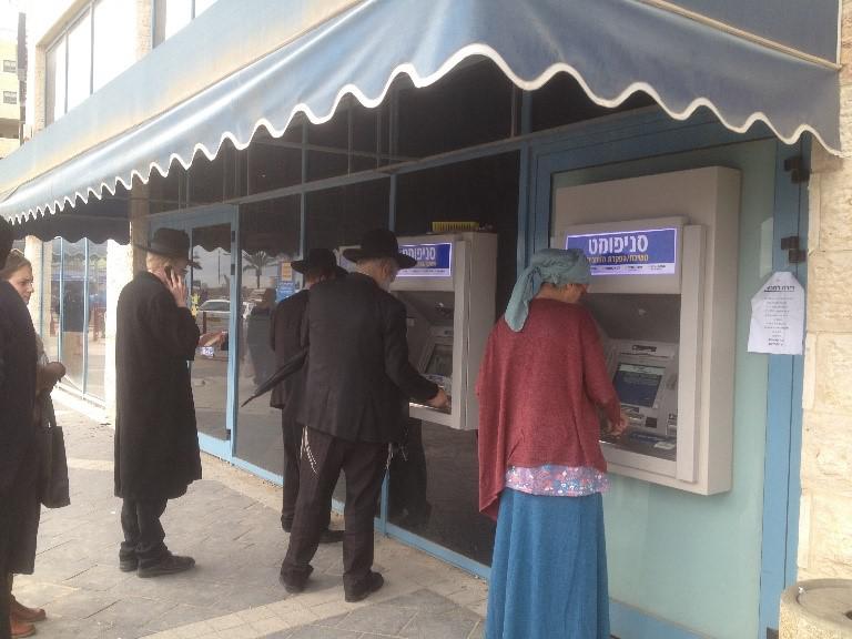 לקוחות משתמשים במסופי בנק אוטומטיים מחוץ לסניף בנק בהתנחלות מודיעין עילית. 