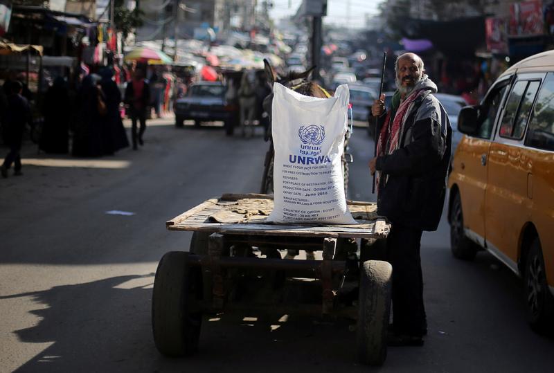 Seorang pria Palestina berdiri di sisi sebuah gerobak yang mengangkut sekarung terigu, disalurkan Badan Pekerjaan dan Pemulihan Perserikatan Bangsa-Bangsa (UNRWA), di kamp pengungsian Khan Younis, Terusan Gaza selatan, 3 Januari 2018. 