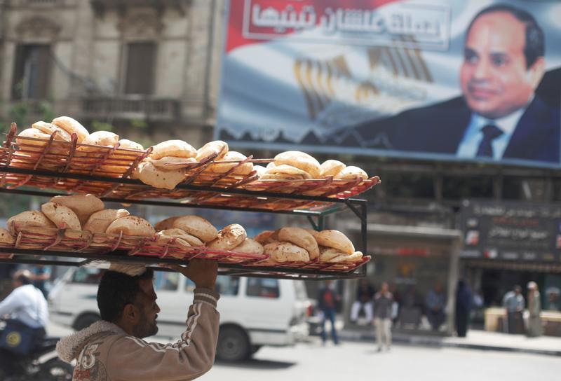 رجل يحمل الخبز على رأسه في شارع مزدحم قرب لافتة للرئيس المصري عبد الفتاح السيسي من حملة "علشان تبنيها" بعد نتائج الانتخابات في القاهرة، مصر، 3 أبريل/نيسان 2018. © 2018 رويترز/ عمرو عبدالله دلش