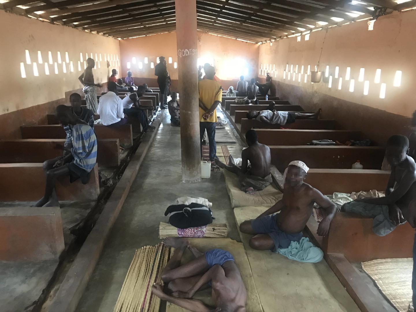 Men sitting on beds and on the floor in a crowded room