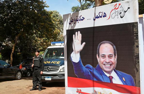 شرطي مصري يحرس قلم اقتراع وبجانبه لافتة انتخابية تحمل صورة الرئيس الحالي عبد الفتاح السيسي مكتوب فوقها باللغة العربية عبارة "من أجل مصر هانكمل... حكاية وطن"، في حي الزمالك في العاصمة القاهرة في 26 مارس/آذار 2018. ©2018 خالد دسوقي/وكالة الصحافة الفرنسية/ غ