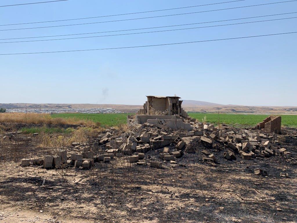 ماڵێکی وێرانە لە نزیک گوندی آەشقەلە السغیر لە حەمدانیە، تەموزی ٢٠١٩. کامپی حەسەن شام لە باکگراوندی وێنەکەدا. © 2019 بەڵقیس وویڵی/ هیومان ڕایتس ۆوچ