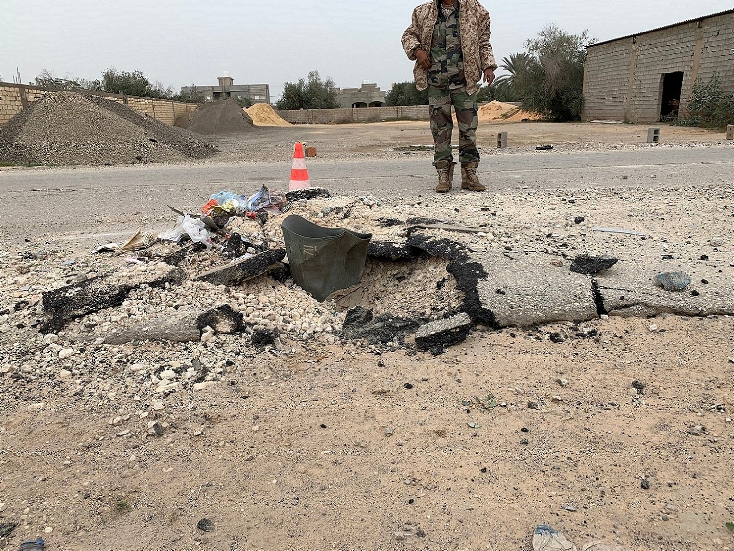 حارس نقطة تفتيش لحكومة الوفاق الوطني يقف خلف حجرة حمولة فارغة من قنبلة عنقودية من طراز "آر بي كيه-250 بي تي آيه بي-2.5 إم" ضربت طريق الأصفاح قرب مطار طرابلس الدولي بعد هجوم في 2 ديسمبر/كانون الأول 2019.