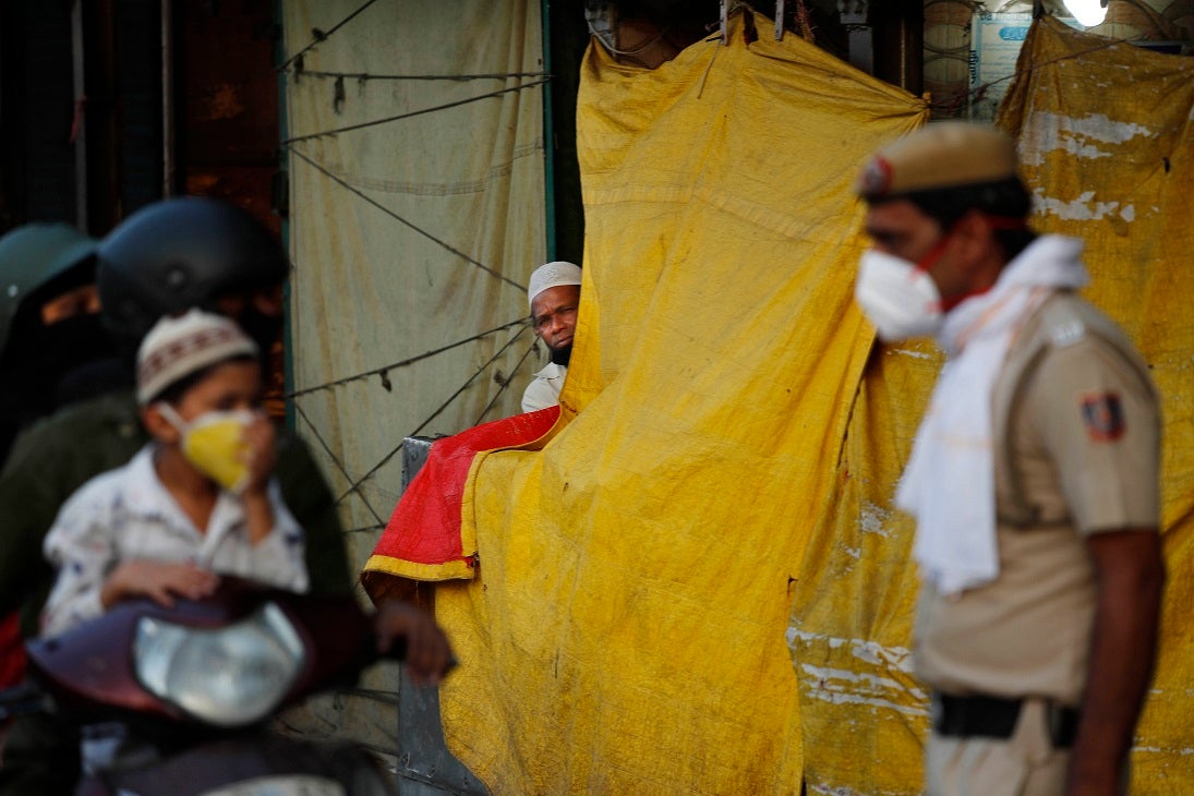 रमज़ान के पवित्र माह के पहला दिन नई दिल्ली के पुराने रिहाइशी इलाके में स्कूटर पर सवार  परिवार को सोशल डिस्टेंसिंग का निर्देश देते पुलिसकर्मी को देखता एक भारतीय मुस्लमान, भारत, 25 अप्रैल, 2020. © 2020 एपी फोटो/मनीष स्वरूप