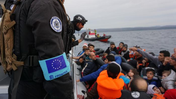 Frontex coast guards talking to group of migrants on boat