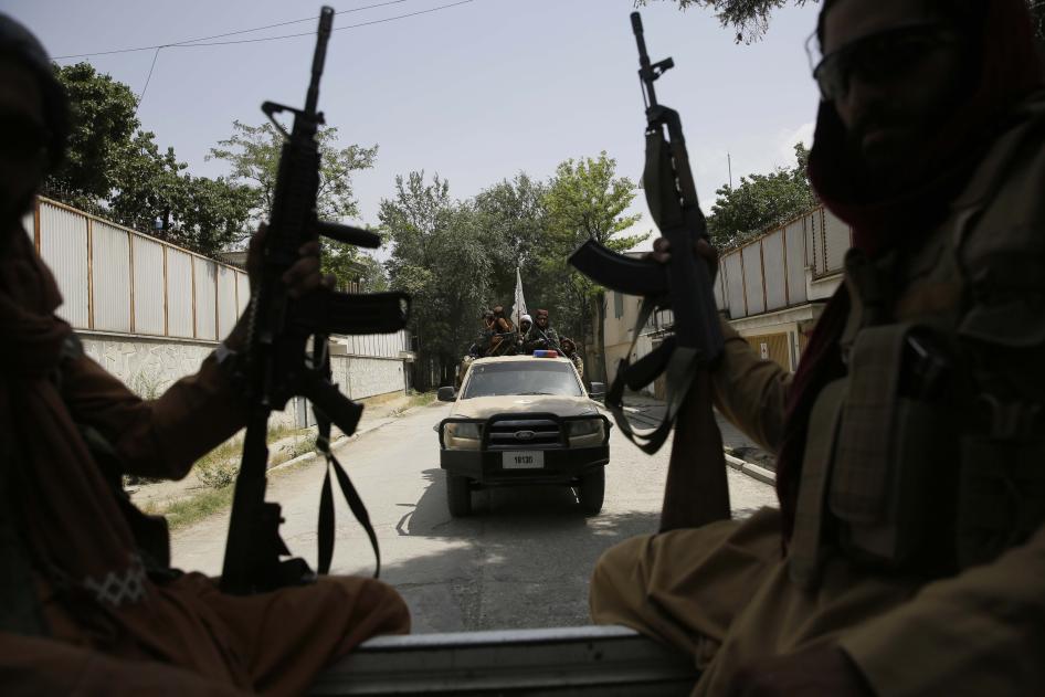 Two men holding weapons ride in the bed of a truck