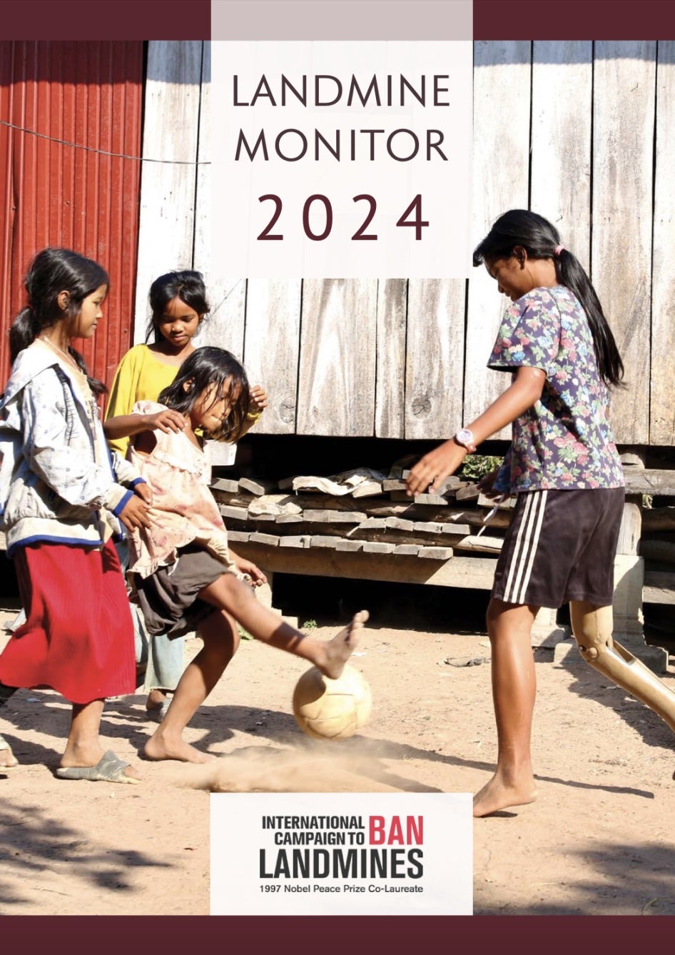 Three young girls play soccer in Cambodia. One girl who lost her leg from a landmine explosion is playing with a prosthetic leg. 