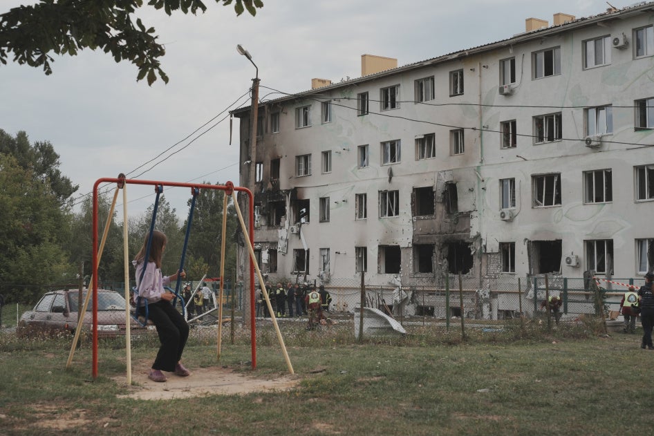 Une petite fille sur une balançoire regarde un immeuble résidentiel dans le quartier Industrialnyi de Kharkiv, en Ukraine, endommagé par une attaque de drone russe qui a tué 7 personnes (dont des enfants) et blessé 23 autres, le 18 août 2025.