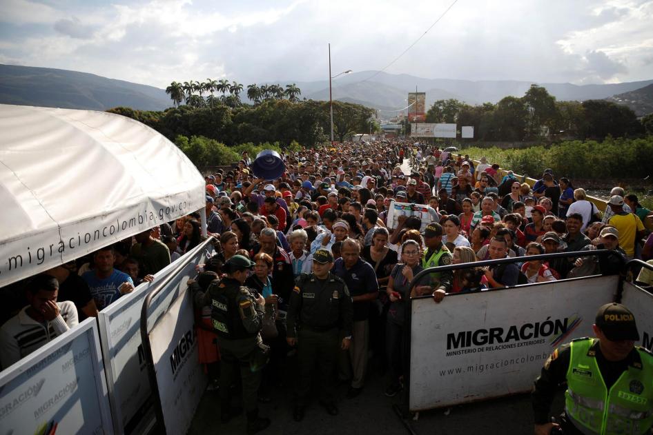 Colombian police officers stand in front of people queueing to try to cross into Colombia from Venezuela through the Simon Bolivar international bridge in Cucuta, Colombia. January 24, 2018.