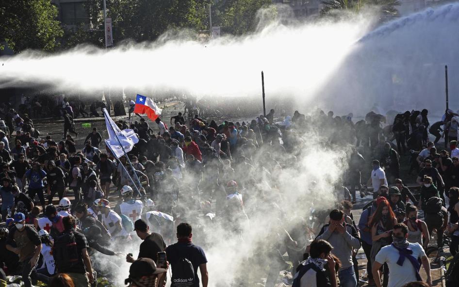 Demonstrators run from police launching water canons and tear gas as a state of emergency remains in effect in Santiago, Chile, Sunday, Oct. 20, 2019. 