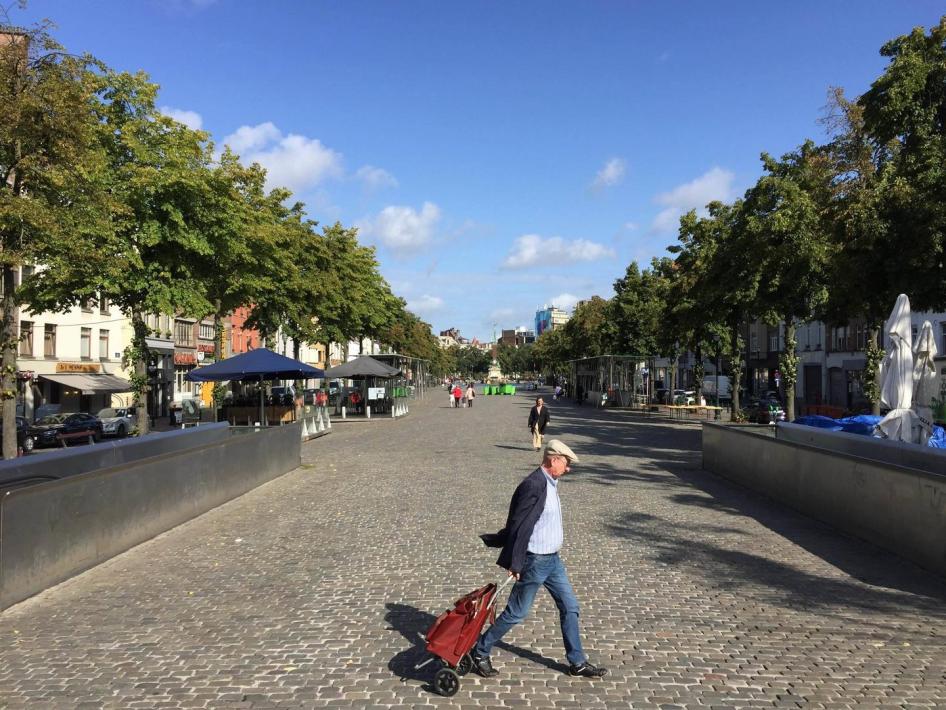 A man with a shopping cart crossing a street on a sunny day