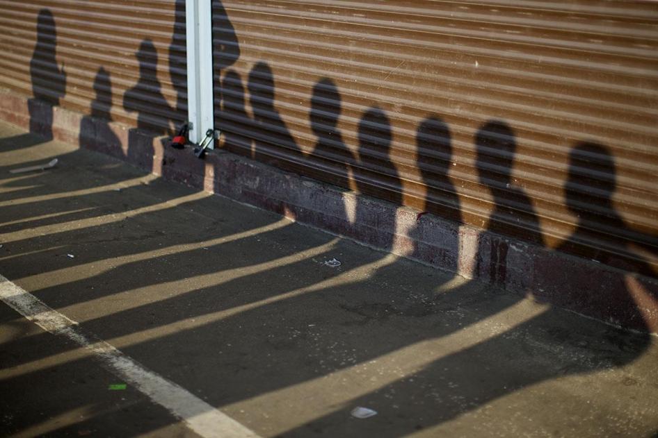 Тени подозреваемых в нарушении миграционных правил людей, видимые на контейнерах рынка в Москве во время задержания сотрудниками полиции 7 августа 2013. © AP Photo/Alexander Zemlianichenko