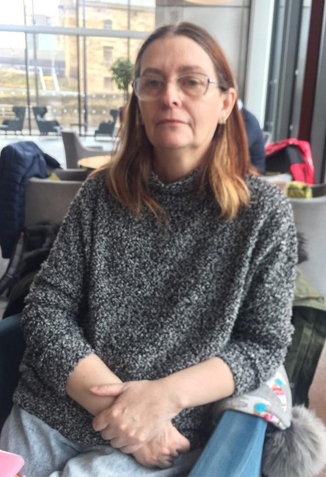 A woman in a gray sweater and glasses poses for the camera