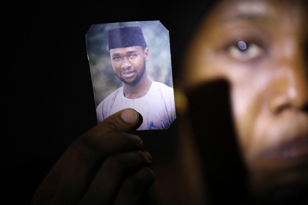A woman holds up a phone with a photo of her husband on it