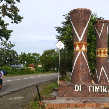 People on a motorcycle ride past a statue of two traditional Papuan wood drums