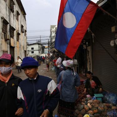 Lao people walk past their country flag, in the capital Vientiane, Laos. 